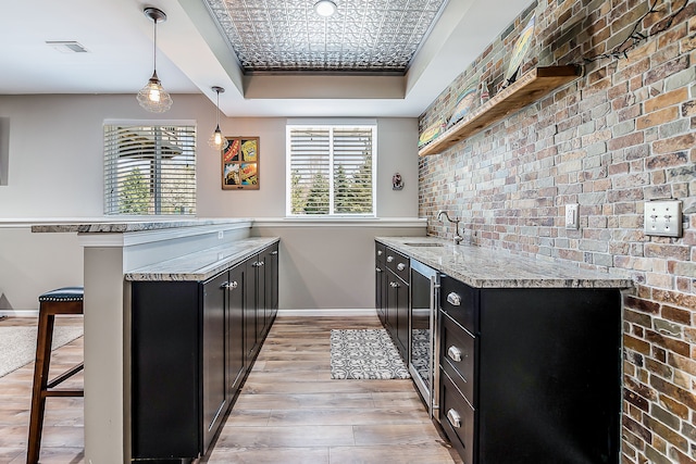kitchen featuring a sink, baseboards, light wood finished floors, a peninsula, and dark cabinetry