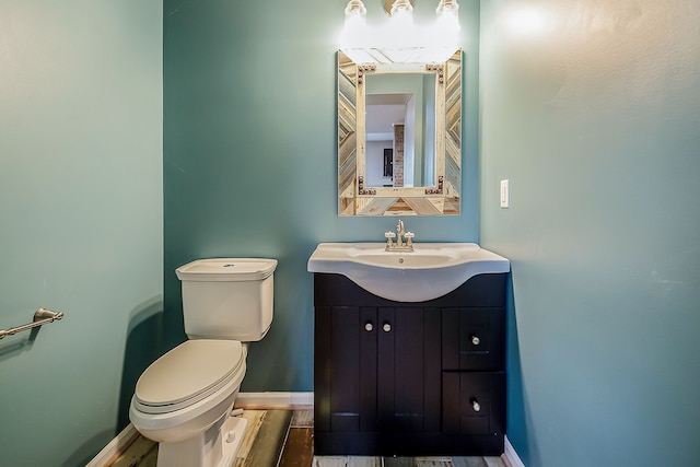 half bath featuring wood finished floors, vanity, toilet, and baseboards