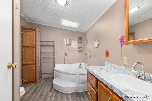 full bathroom featuring wood finished floors, a textured ceiling, ornamental molding, vanity, and a garden tub