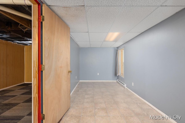 finished below grade area featuring a drop ceiling, a baseboard heating unit, and baseboards
