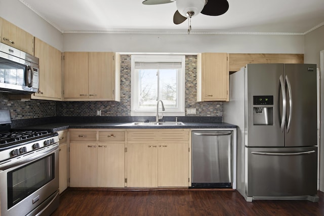 kitchen with light brown cabinetry, stainless steel appliances, dark countertops, and a sink