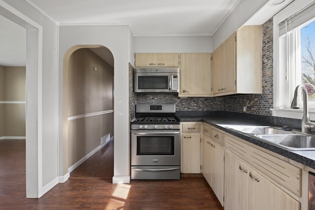 kitchen featuring cream cabinets, stainless steel appliances, backsplash, a sink, and dark wood-style floors