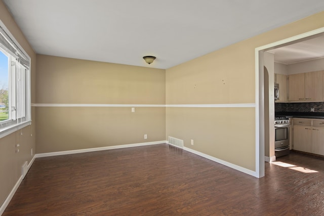 unfurnished room with dark wood-style flooring, visible vents, and baseboards