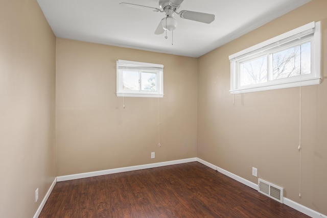 unfurnished room with visible vents, a ceiling fan, a healthy amount of sunlight, and dark wood-type flooring
