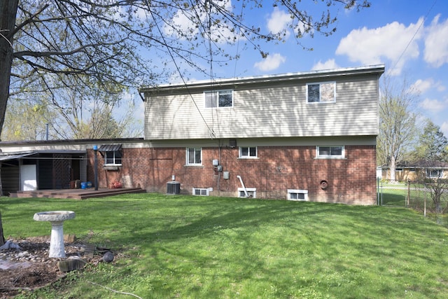 back of property featuring brick siding, fence, central AC unit, and a yard