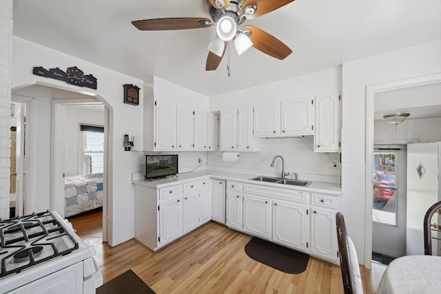 kitchen with arched walkways, white gas stove, white cabinetry, and a sink
