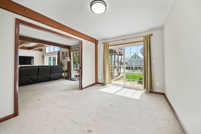 spare room with carpet flooring, beamed ceiling, plenty of natural light, and baseboards