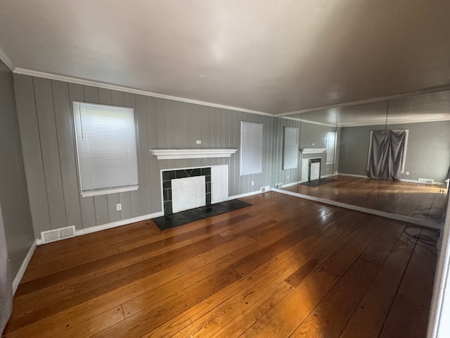 unfurnished living room featuring a tiled fireplace, visible vents, baseboards, ornamental molding, and hardwood / wood-style floors