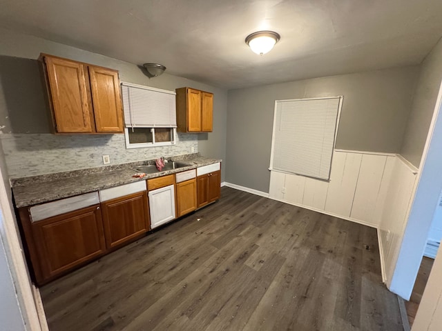 kitchen with a sink, dark wood-style flooring, brown cabinets, decorative backsplash, and wainscoting
