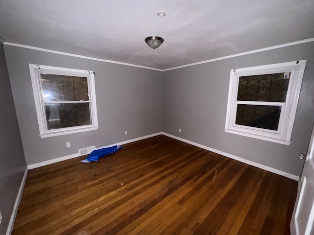 unfurnished room with crown molding, visible vents, baseboards, and dark wood-type flooring