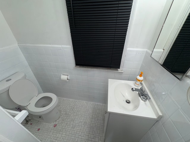 half bathroom with a wainscoted wall, toilet, tile walls, tile patterned floors, and vanity