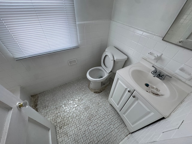 bathroom with toilet, tile walls, wainscoting, and vanity