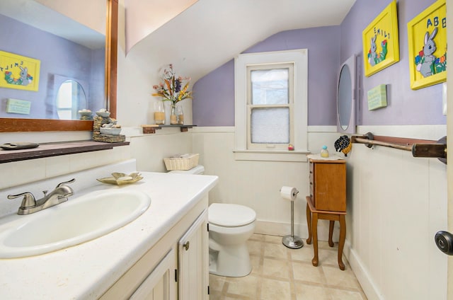 bathroom with vanity, wainscoting, toilet, tile patterned floors, and vaulted ceiling