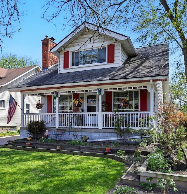 view of front of property with a shingled roof, a front lawn, and covered porch