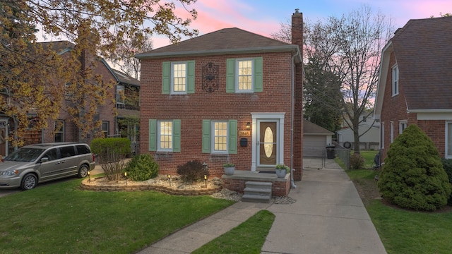 view of front of house with a chimney, a yard, brick siding, and a garage