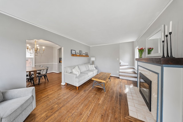 living area with arched walkways, ornamental molding, a fireplace, wood finished floors, and a notable chandelier
