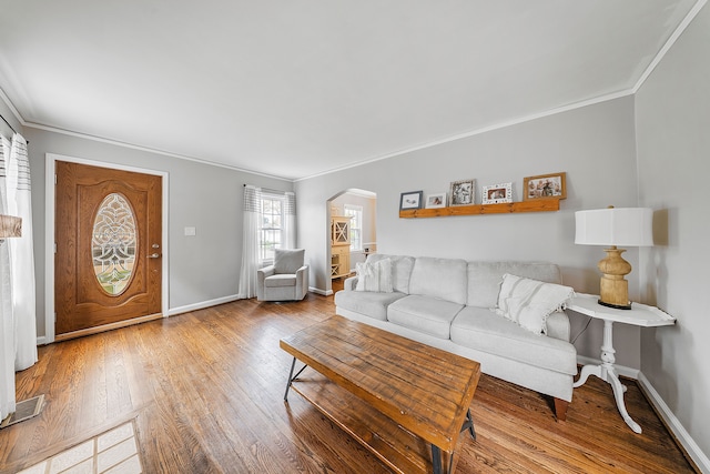 living room with wood finished floors, baseboards, ornamental molding, and arched walkways
