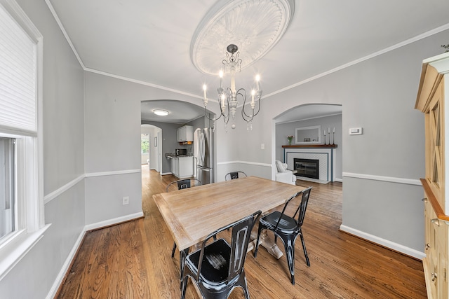 dining area featuring wood finished floors, baseboards, ornamental molding, and arched walkways