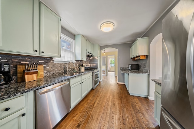 kitchen featuring decorative backsplash, a sink, appliances with stainless steel finishes, arched walkways, and dark wood-type flooring