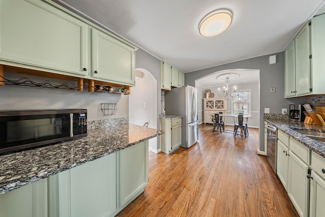 kitchen featuring arched walkways, an inviting chandelier, green cabinetry, light wood-style floors, and appliances with stainless steel finishes