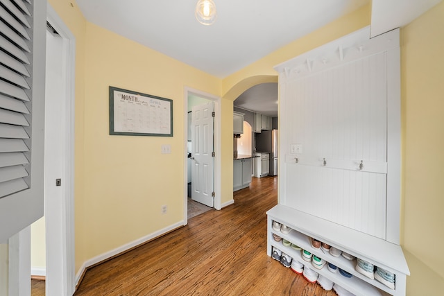 hallway with arched walkways, wood finished floors, and baseboards