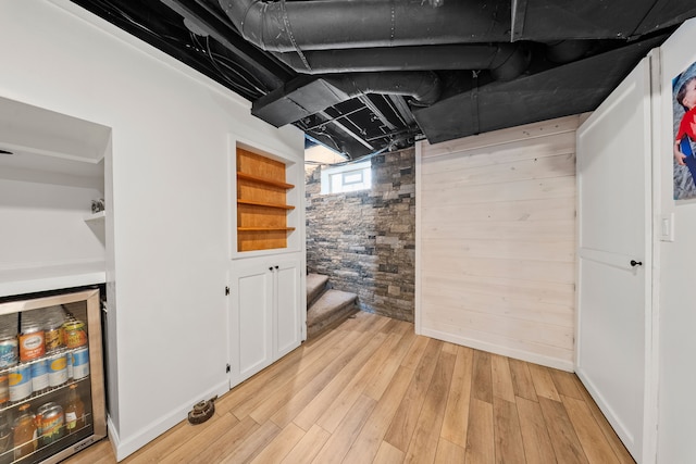 basement with beverage cooler, stairway, wood walls, baseboards, and light wood-type flooring