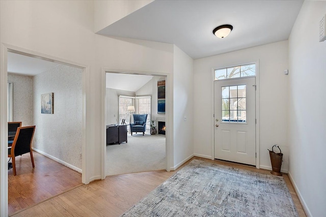 entryway featuring light wood-style floors, baseboards, lofted ceiling, and a lit fireplace