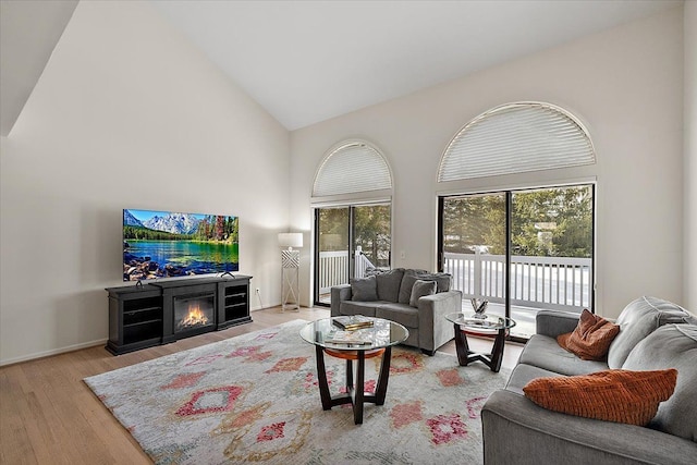 living area with light wood-style flooring, a glass covered fireplace, and high vaulted ceiling