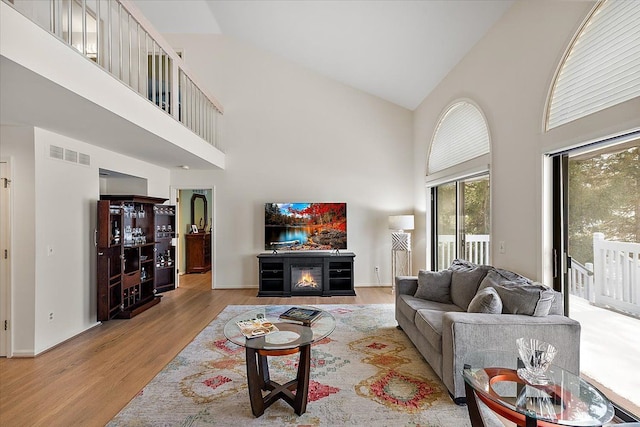 living area featuring visible vents, a glass covered fireplace, wood finished floors, baseboards, and high vaulted ceiling