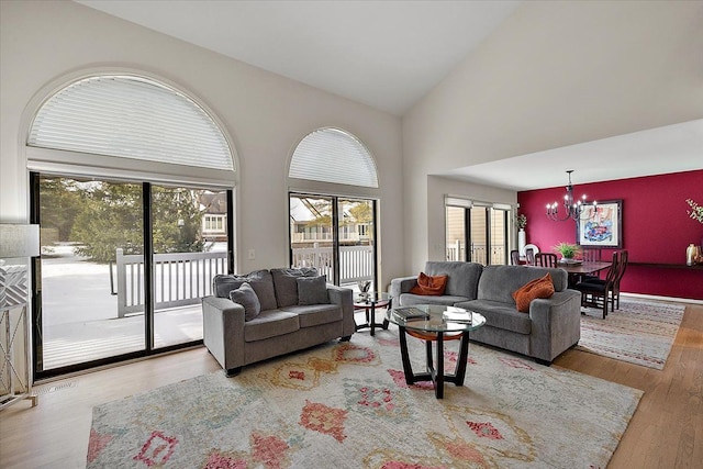 living area featuring high vaulted ceiling, wood finished floors, a notable chandelier, and a wealth of natural light