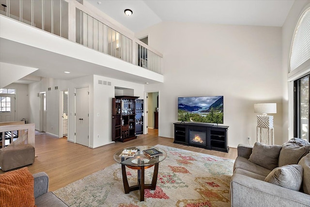living area with wood finished floors, a glass covered fireplace, a high ceiling, and visible vents