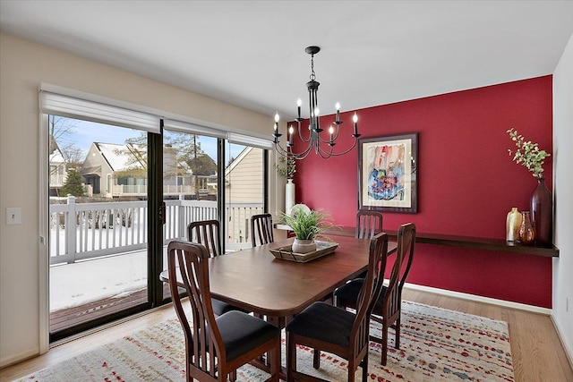 dining area featuring baseboards, light wood finished floors, an accent wall, and a chandelier