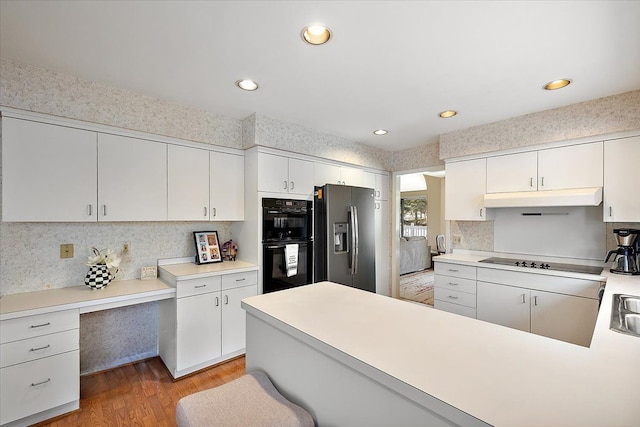 kitchen featuring light countertops, a peninsula, light wood-type flooring, under cabinet range hood, and black appliances