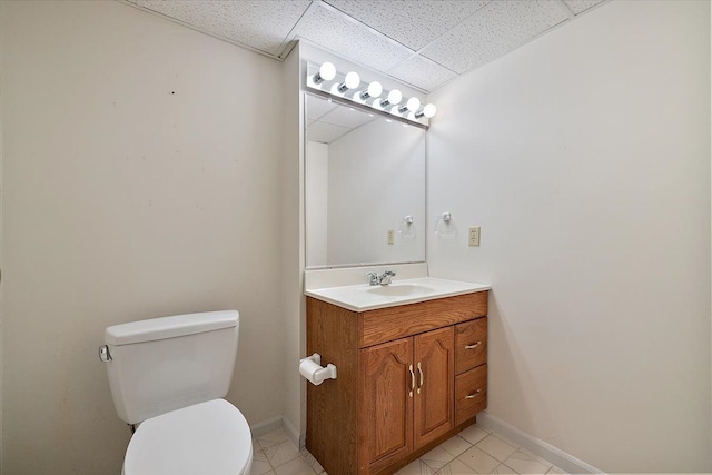 half bathroom with vanity, baseboards, toilet, and a paneled ceiling
