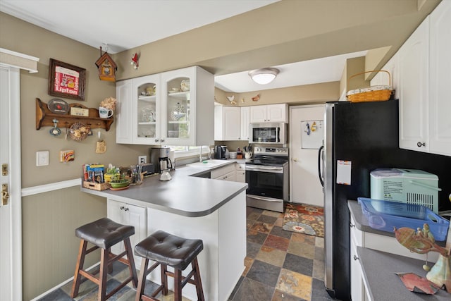 kitchen featuring stone finish flooring, appliances with stainless steel finishes, a sink, a peninsula, and glass insert cabinets