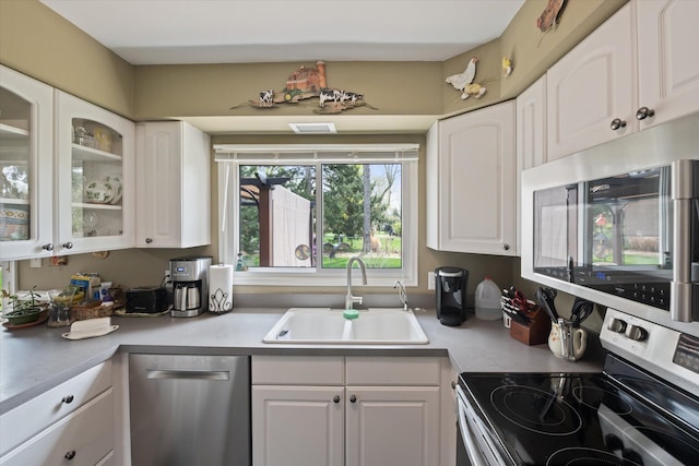kitchen featuring glass insert cabinets, light countertops, white cabinets, a sink, and stainless steel appliances