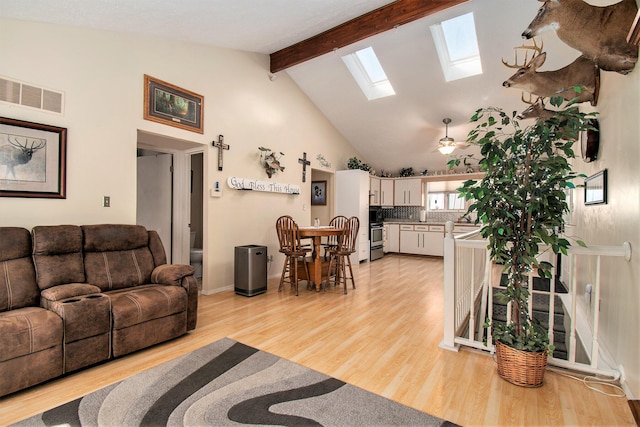 living area featuring beamed ceiling, high vaulted ceiling, light wood-type flooring, visible vents, and a skylight