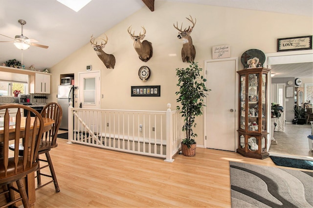 dining space with a ceiling fan, vaulted ceiling with skylight, and light wood-style floors