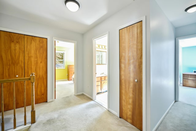 corridor with baseboards and light colored carpet
