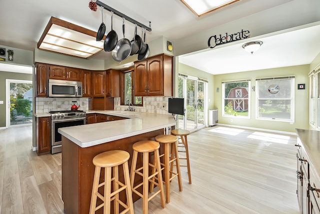 kitchen featuring tasteful backsplash, stainless steel appliances, light countertops, a sink, and light wood-type flooring