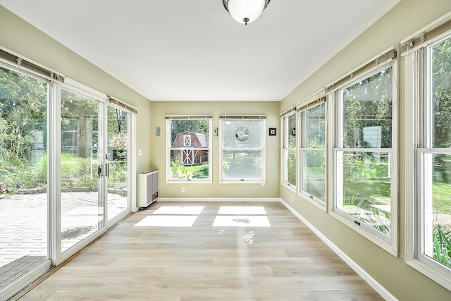 unfurnished sunroom with a wealth of natural light, wood finished floors, french doors, and baseboards