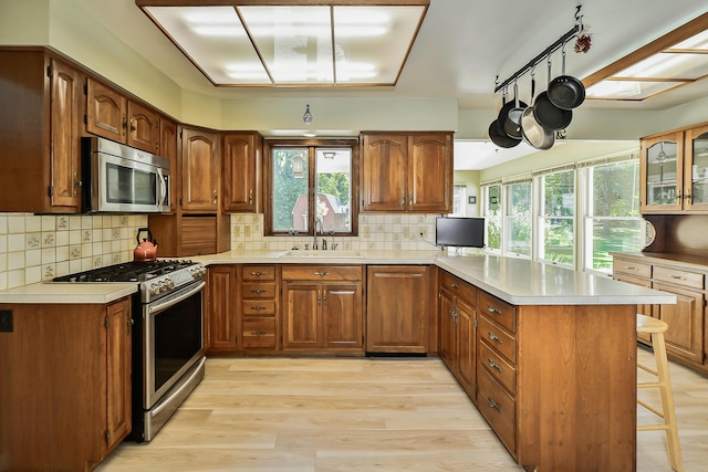 kitchen with a sink, stainless steel appliances, a kitchen breakfast bar, light wood-type flooring, and a peninsula