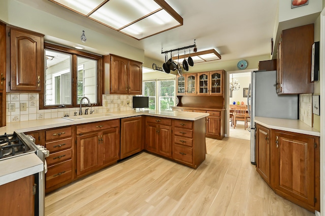 kitchen with tasteful backsplash, light wood-style floors, appliances with stainless steel finishes, brown cabinets, and a sink