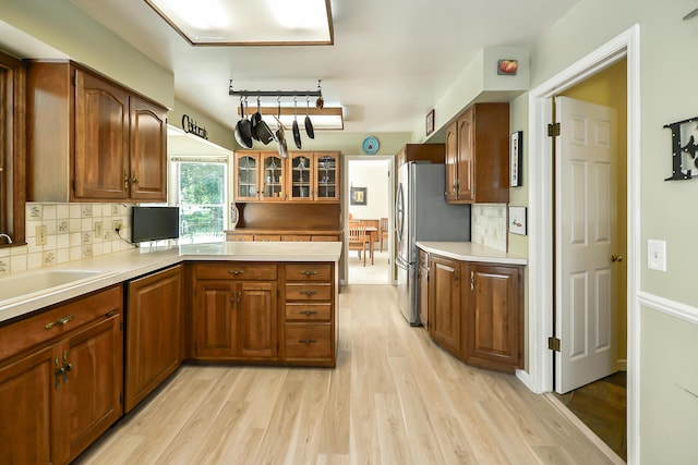 kitchen with decorative backsplash, light wood-style floors, glass insert cabinets, a peninsula, and freestanding refrigerator