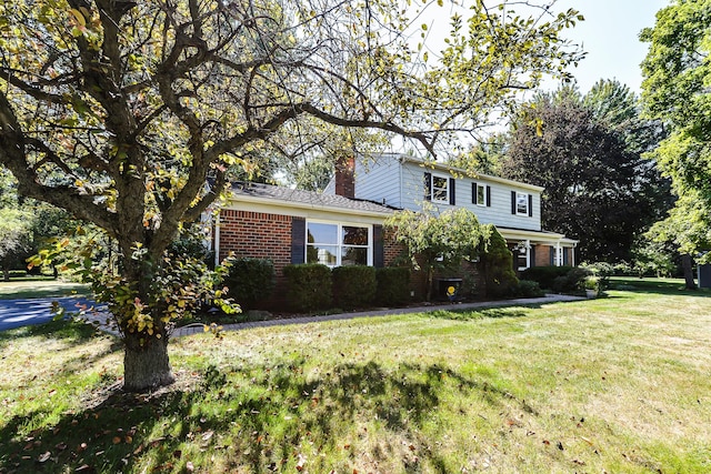 traditional-style house featuring a front lawn, a chimney, and brick siding