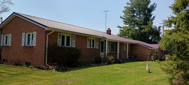 exterior space featuring a chimney, brick siding, a front lawn, and metal roof