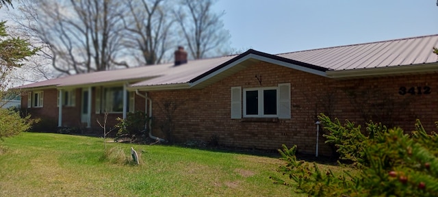 exterior space featuring a chimney, brick siding, metal roof, and a lawn
