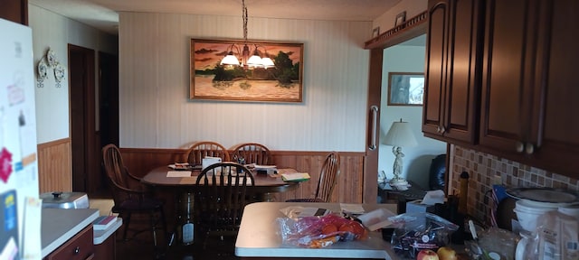 dining space featuring wooden walls, a notable chandelier, and wainscoting