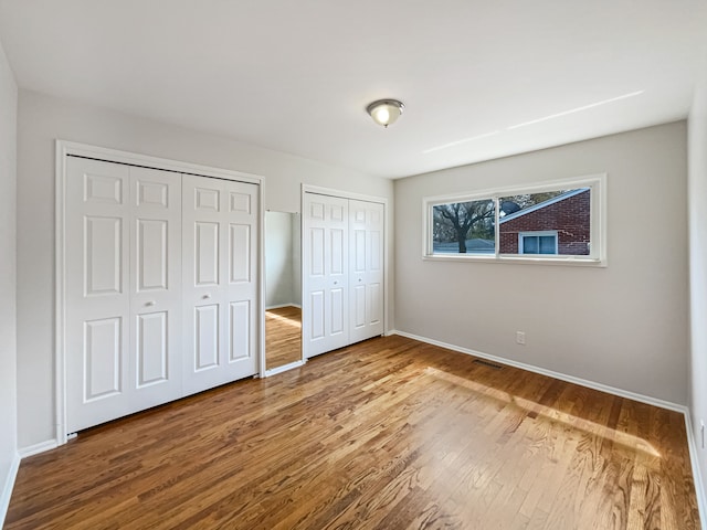 unfurnished bedroom featuring two closets, baseboards, visible vents, and wood finished floors