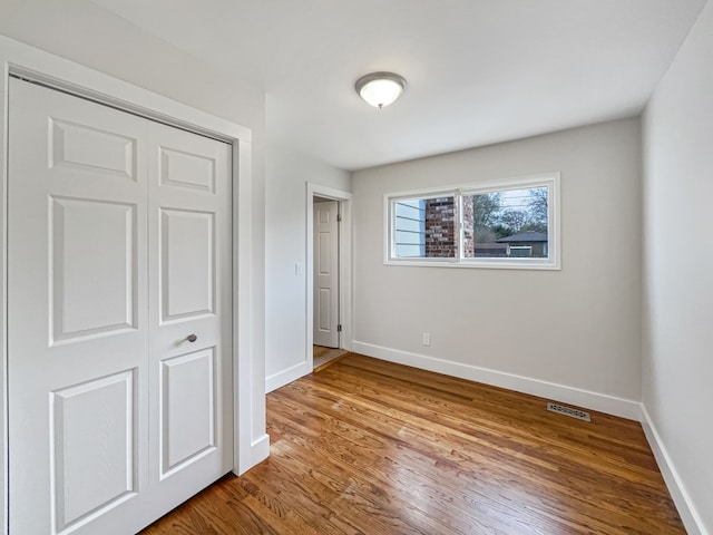 unfurnished bedroom featuring baseboards, a closet, wood finished floors, and visible vents